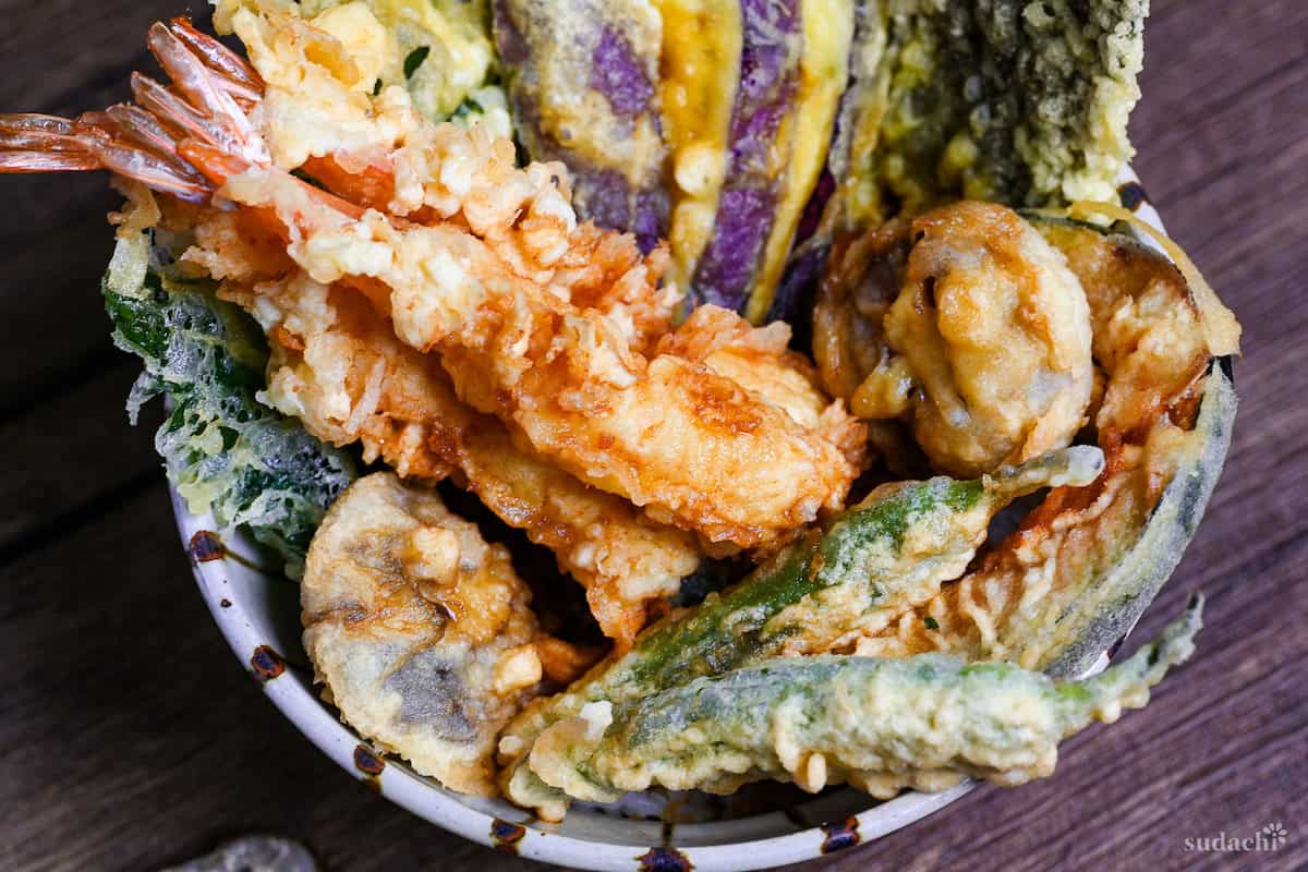 Tendon (Tempura Rice Bowl) made with shrimp and a variety of vegetables in a striped bowl on a wooden surface