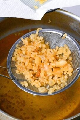 scooping crispy tenkasu tempura flakes out of hot oil using a mesh spoon