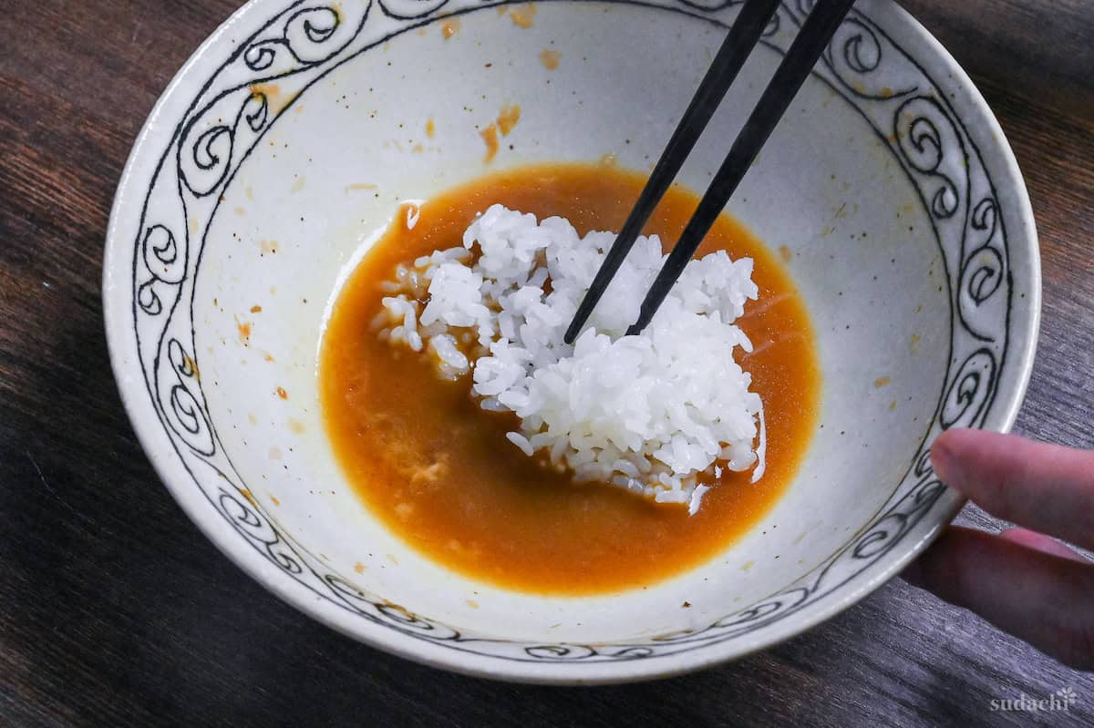 Mixing cooked Japanese rice into leftover TKM sauce with black chopsticks