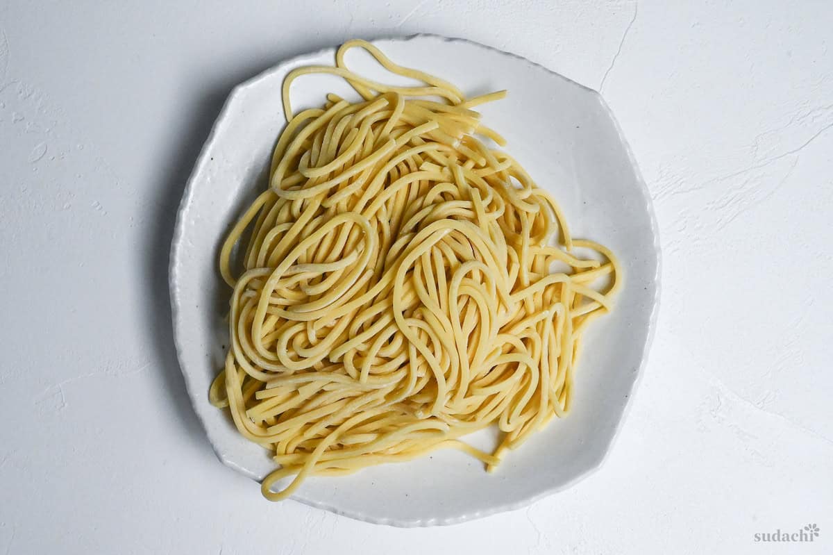 Raw thick ramen noodles for tsukemen on a white plate on a white background top down