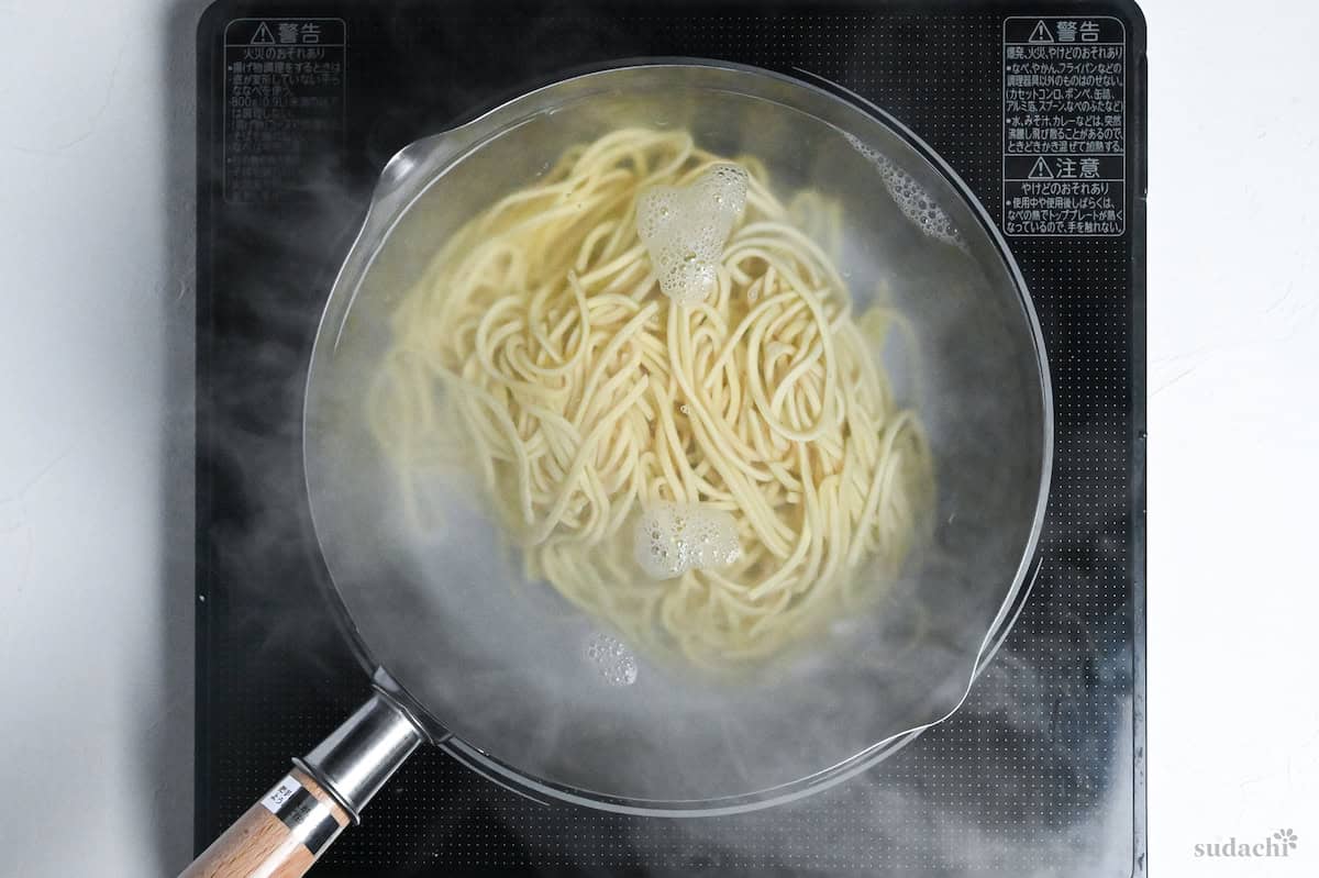 Thick ramen noodles for tsukemen boiling in a pot of water on an IC stovetop