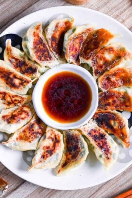pan-fried tofu and vegetable gyoza on a white plate arranged in a circle around a bowl of gyoza dipping sauce