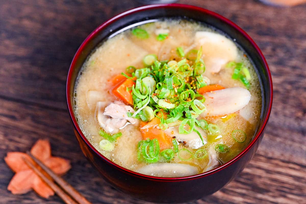 Japanese "Tonjiru" pork miso soup in a black and red bowl topped with shichimi togarashi (chili powder) and green onions