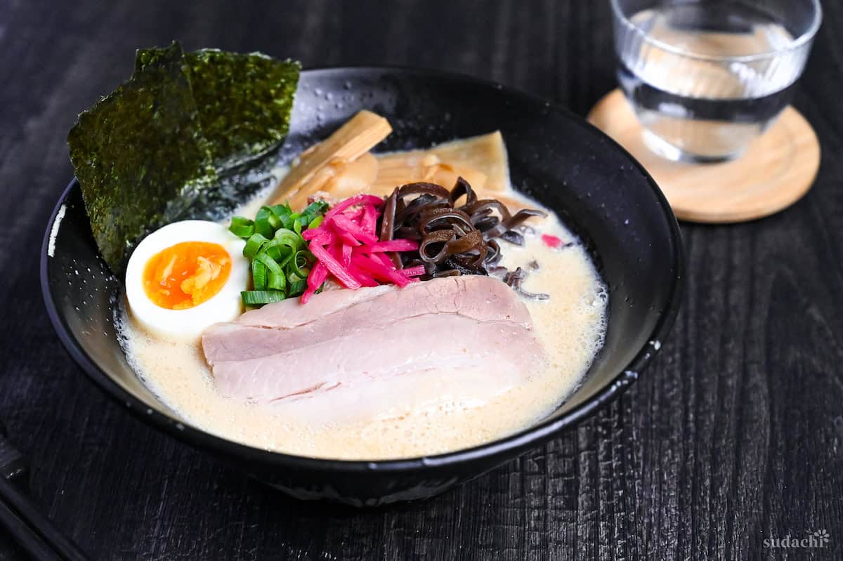easy shortcut tonkotsu-style ramen topped with pork chashu, ramen egg and shredded vegetables in a black bowl on black wood-effect background