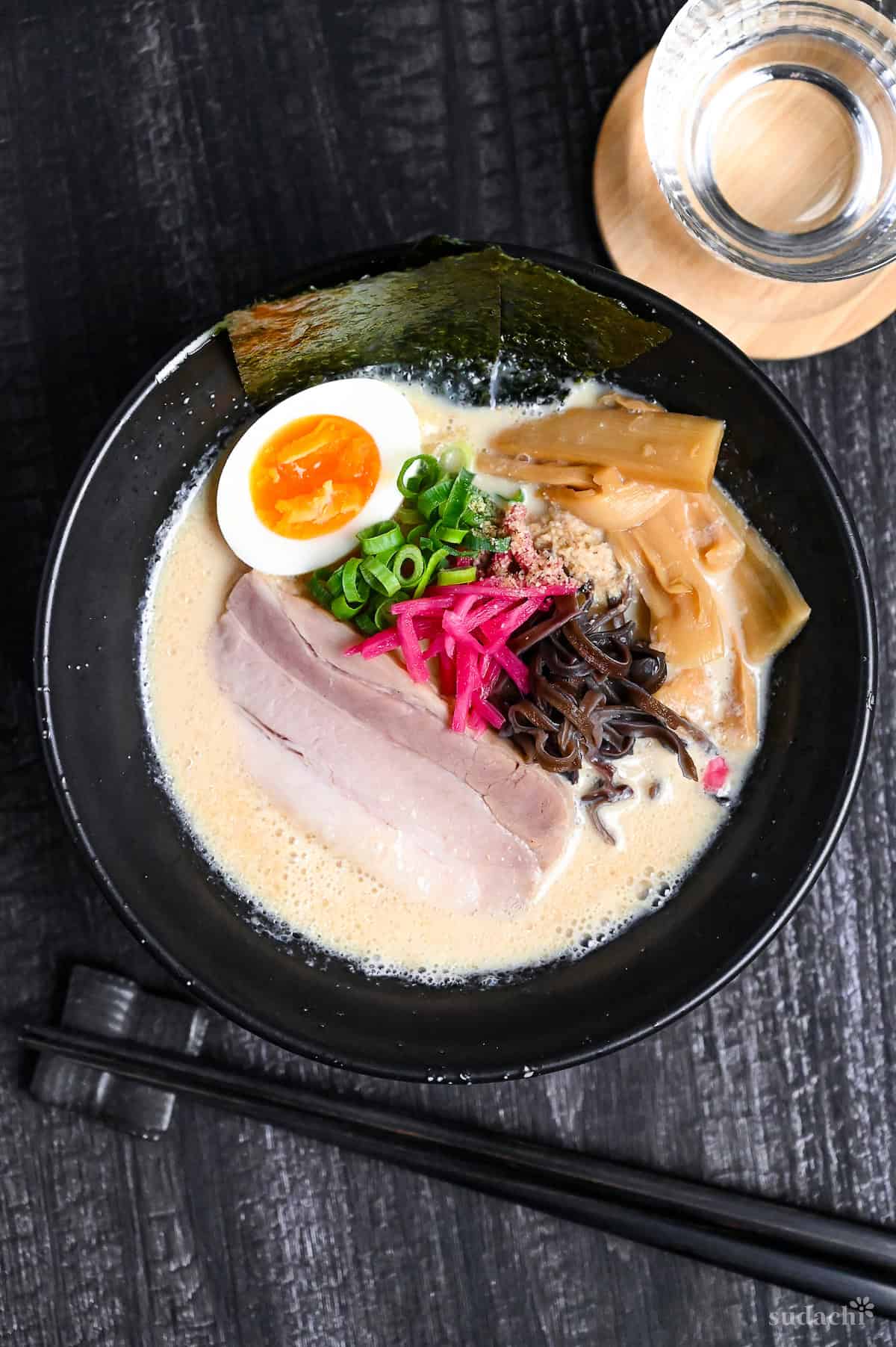 easy shortcut tonkotsu-style ramen topped with pork chashu, ramen egg and shredded vegetables in a black bowl on black wood-effect background