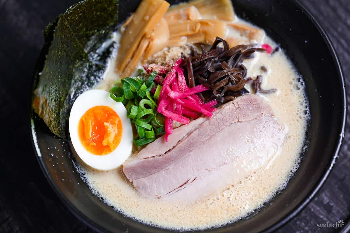 easy shortcut tonkotsu-style ramen topped with pork chashu, ramen egg and shredded vegetables in a black bowl on black wood-effect background
