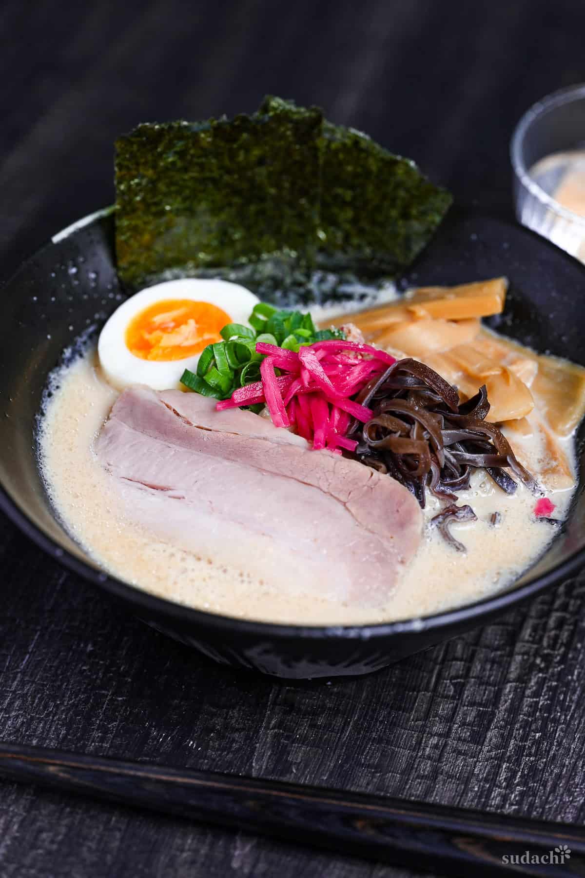 easy shortcut tonkotsu-style ramen topped with pork chashu, ramen egg and shredded vegetables in a black bowl on black wood-effect background