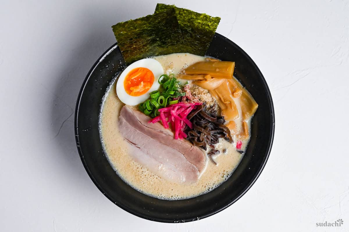 easy shortcut tonkotsu-style ramen topped with pork chashu, ramen egg and shredded vegetables in a black bowl on a white background