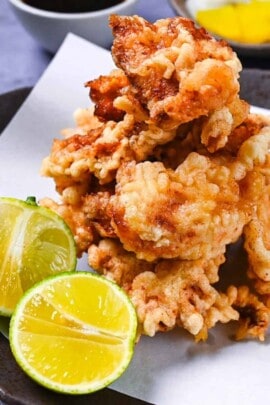 toriten (chicken tempura) piled up on a brown plate with two halves of kabosu citrus