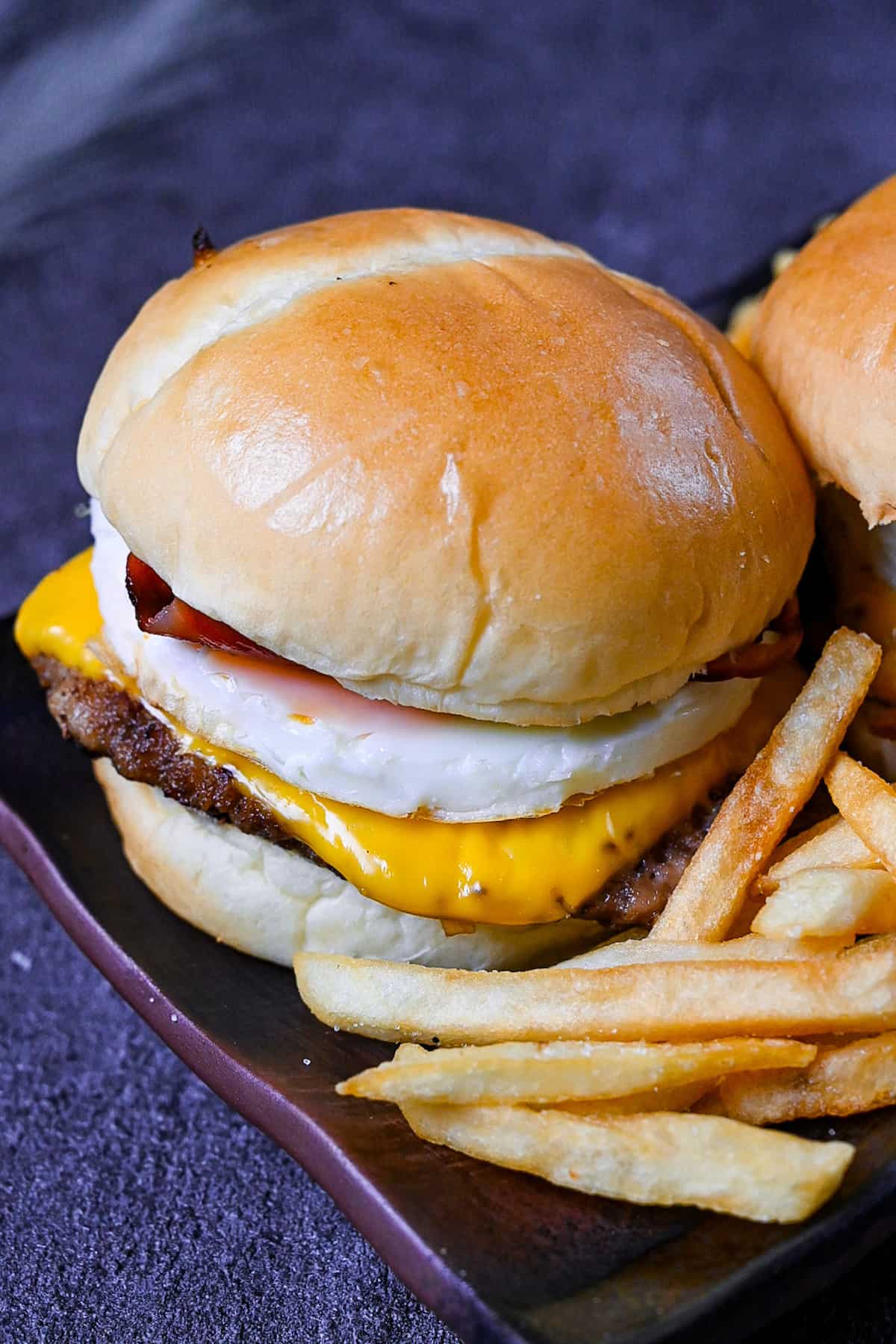 Japanese tsukimi burger on a brown rectangular plate with fries