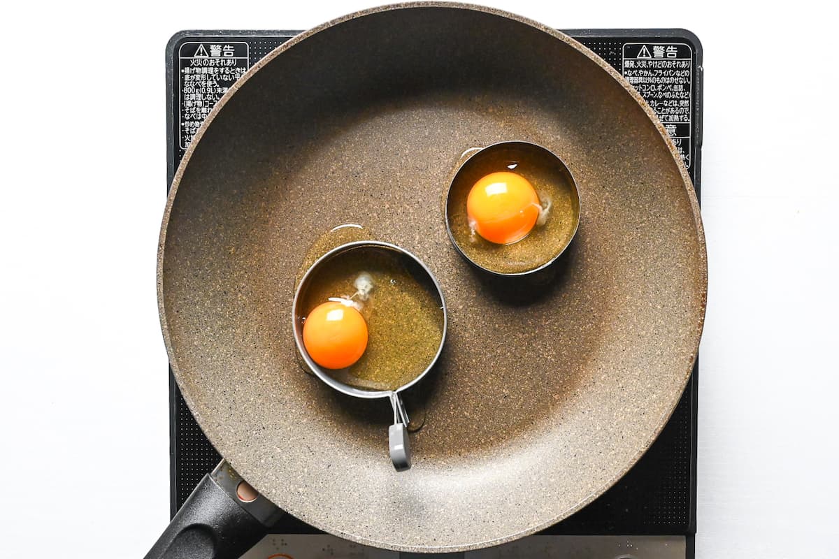 two eggs in round molds in a frying pan