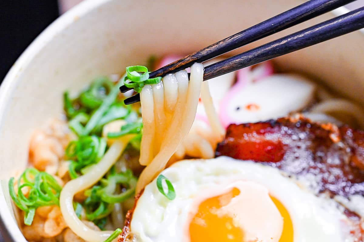 Tsukimi udon made with thick noodles in a dashi broth topped with eggs, bacon, green onion, tempura bits and kamaboko fishcake shaped into a rabbit