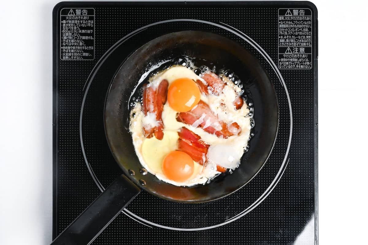 frying bacon and eggs in a pan
