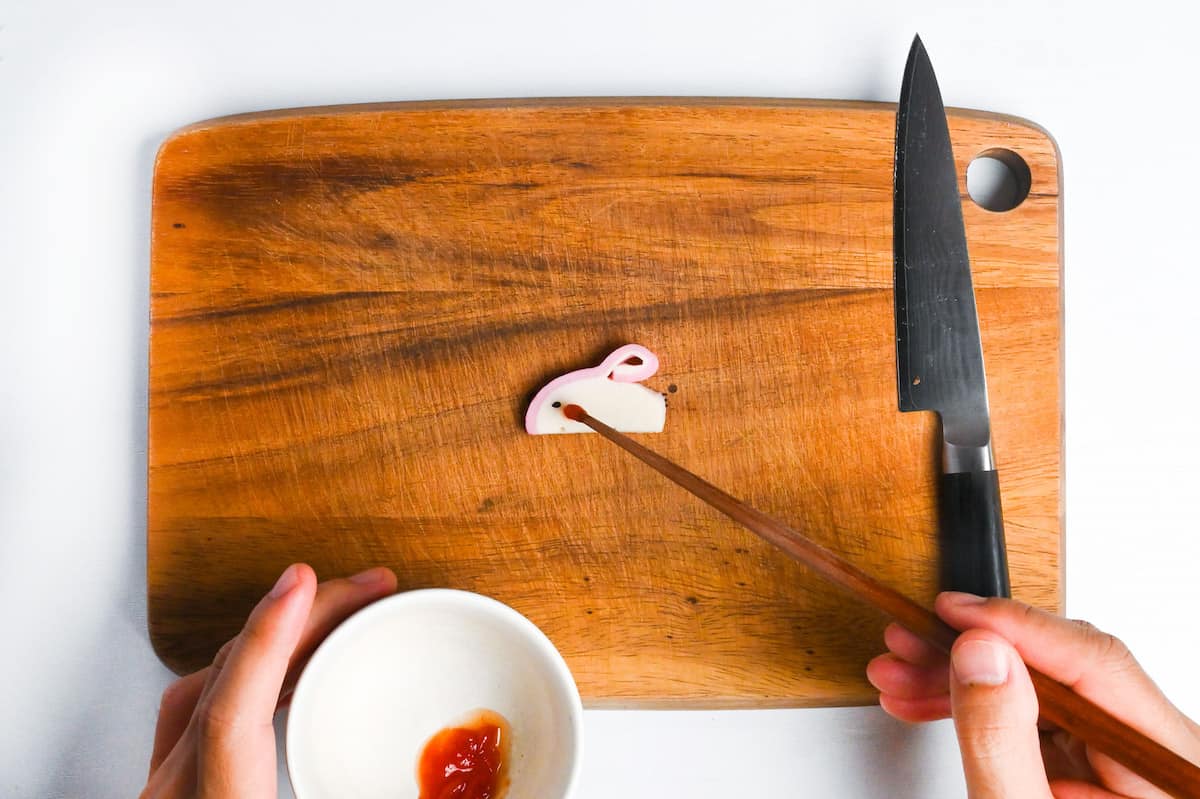 placing one black sesame seed and a small blob of ketchup on kamaboko to make a rabbit
