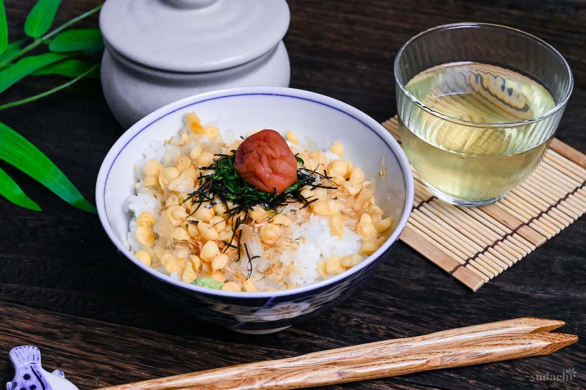 Ume Chazuke in a blue bowl with flower design next to a glass of chilled green tea on a bamboo mat coaster