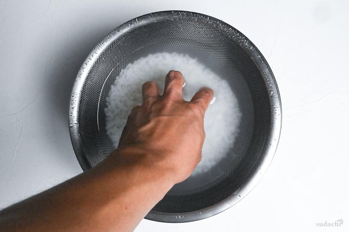 washing rice in a sieve over a bowl of cold water