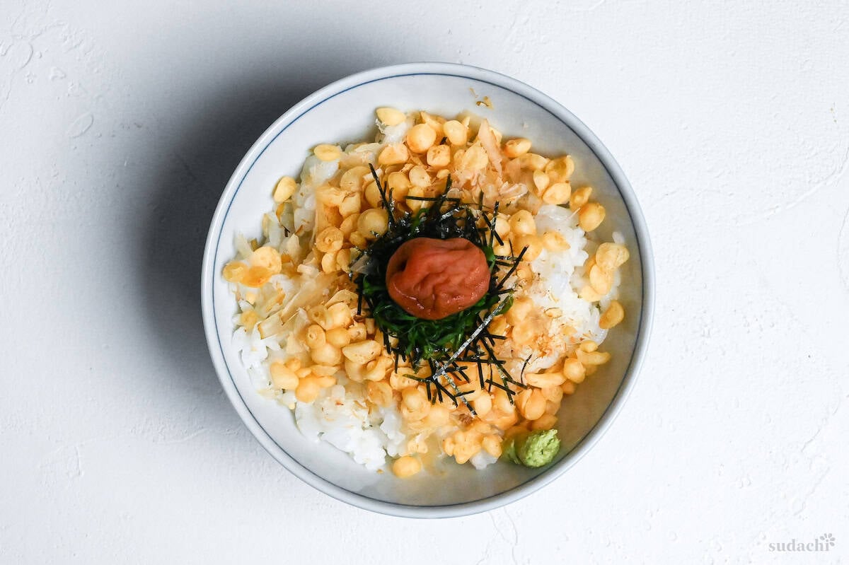 Cold rice topped with tempura flakes, bonito flakes, shredded nori, shredded shiso leaves, a blob of wasabi and a pickled plum in the center