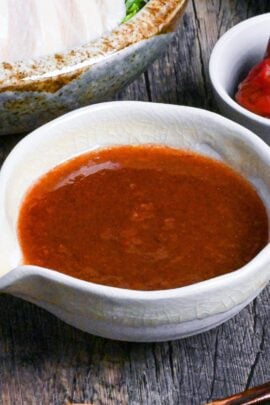 Umeboshi dressing in a cream ceramic pouring bowl with chicken salad and umeboshi in the background