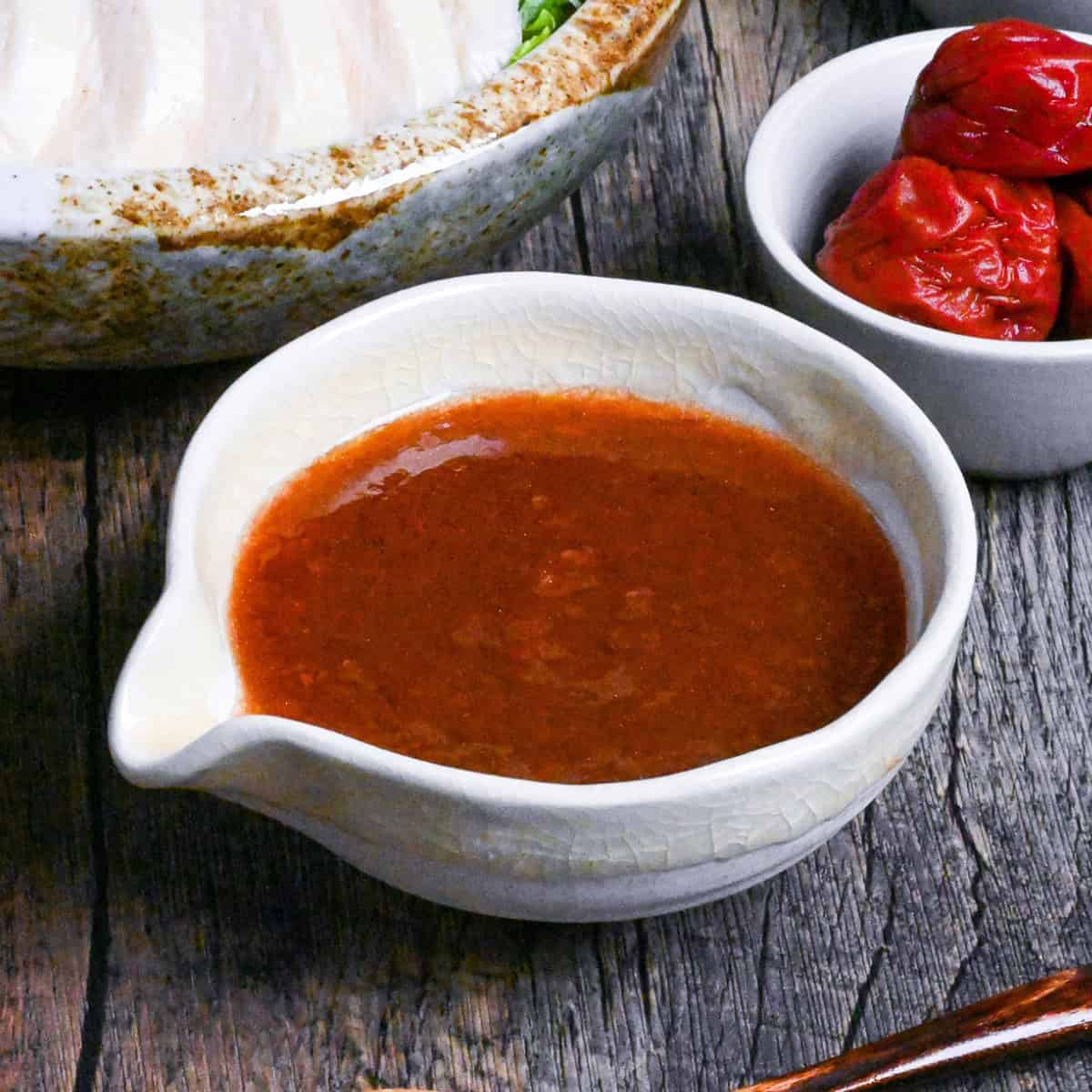 Umeboshi dressing in a cream ceramic pouring bowl with chicken salad and umeboshi in the background