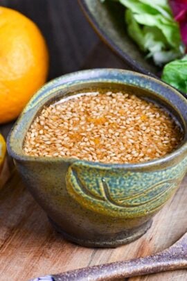 Japanese wafu dressing made with soy sauce and yuzu in a miniature green ceramic jug next to fresh fuzu and a bowl of mixed leaf salad