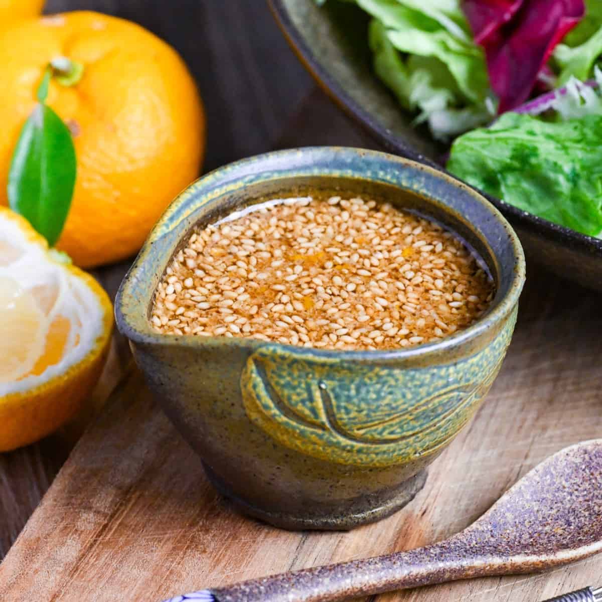 Japanese wafu dressing made with soy sauce and yuzu in a miniature green ceramic jug next to fresh fuzu and a bowl of mixed leaf salad