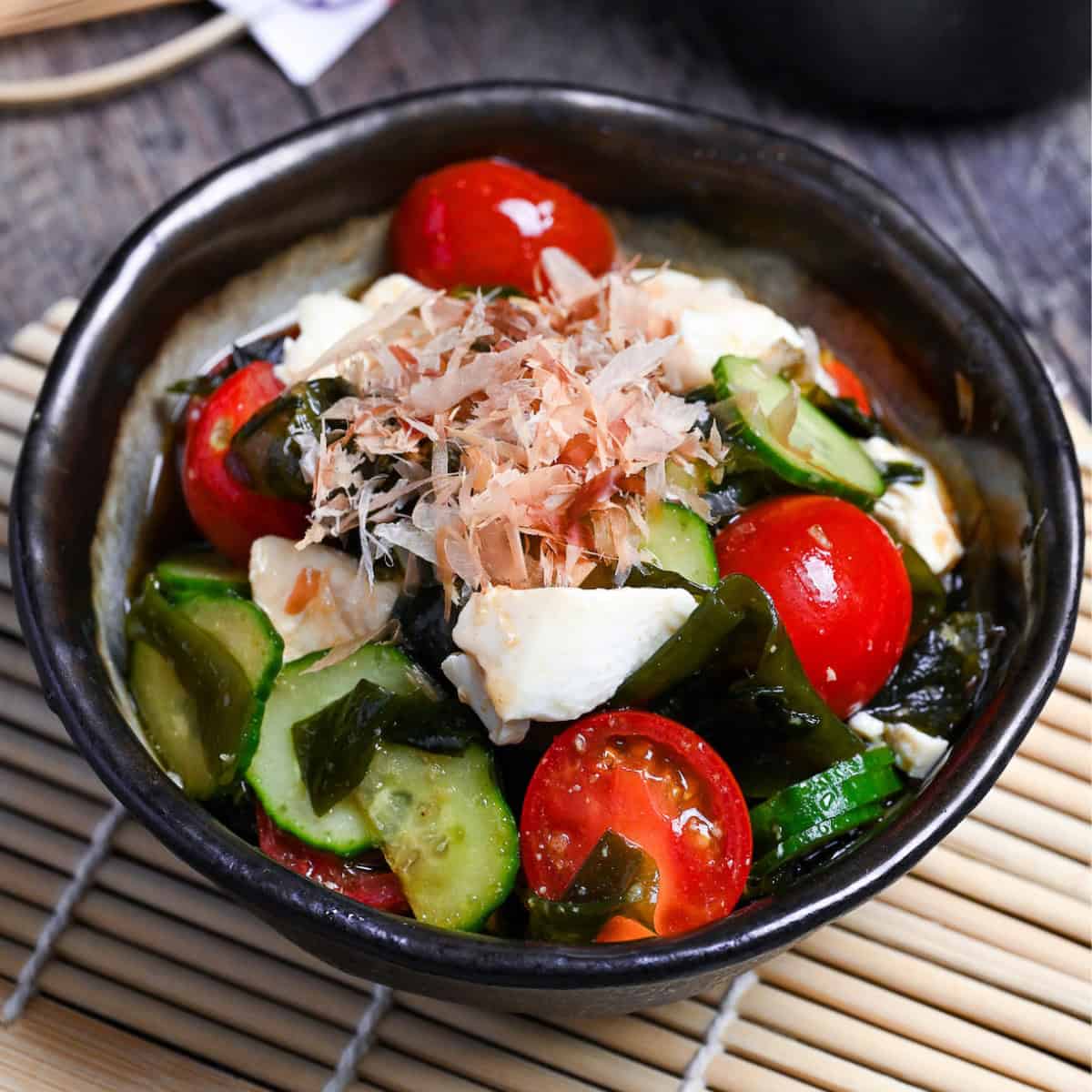 Japanese wakame salad made with wakame seaweed, mini tomatoes, cucumber and silken tofu served in a mottled gray bowl with dark brown edge
