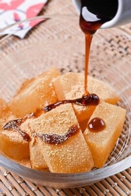 Homemade warabi mochi in a glass bowl coated with kinako and drizzled with kuromitsu syrup