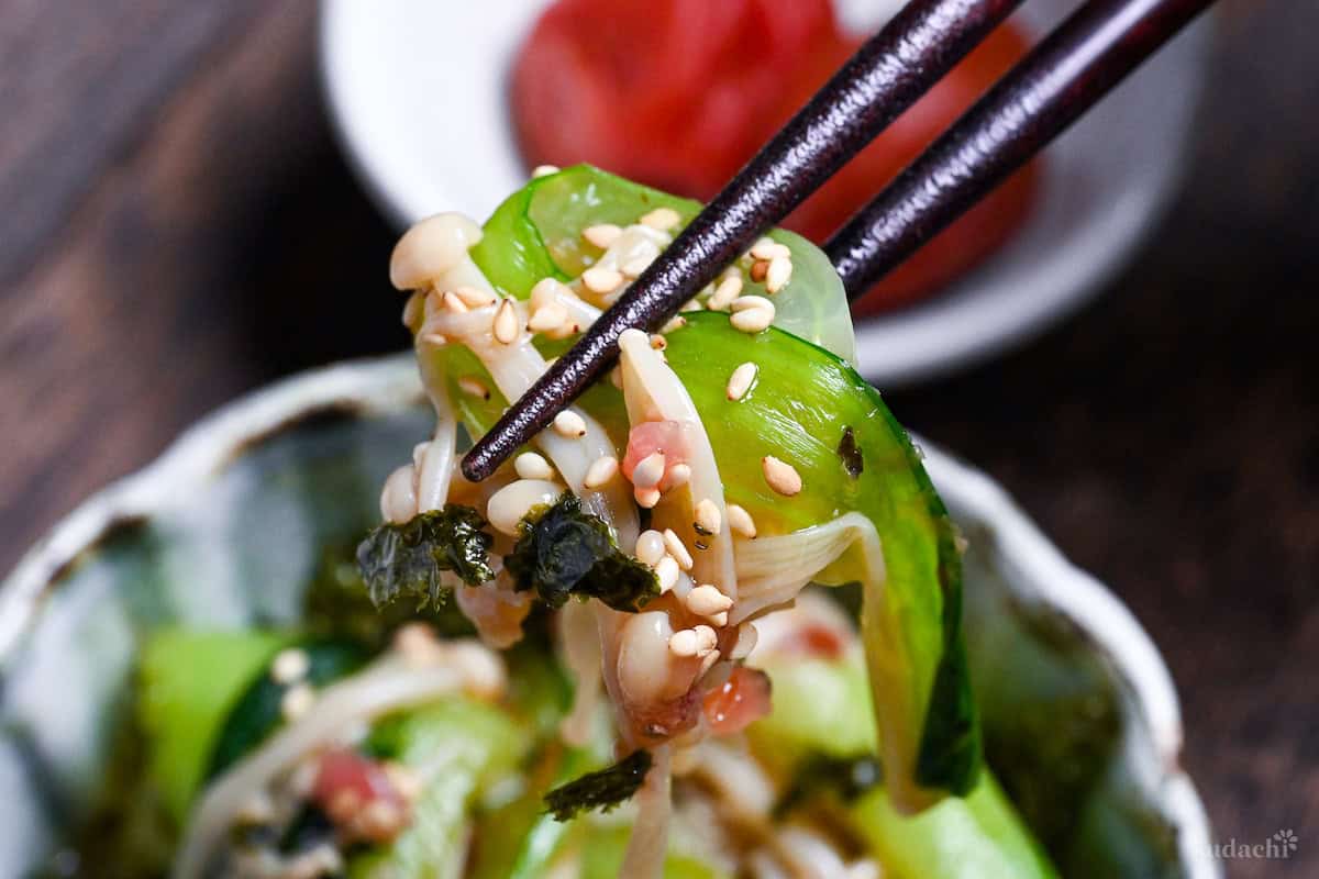 Wasabi-Ae salad with enoki mushrooms and bok choy held up with chopsticks close up