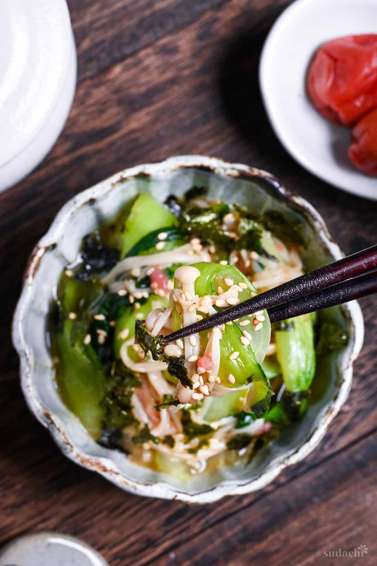 Wasabi-Ae salad with enoki mushrooms and bok choy held up with dark wooden chopsticks