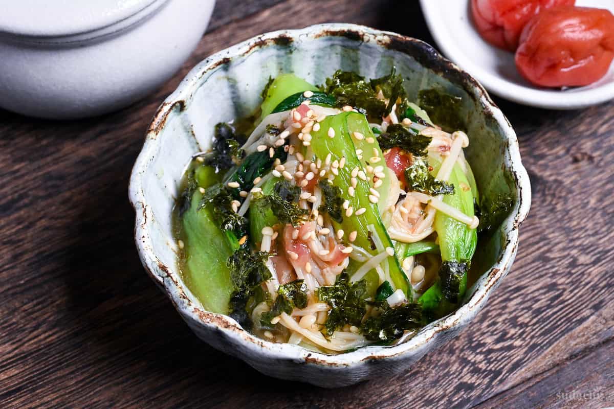 Wasabi-Ae salad with enoki mushrooms and bok choy in a blue and brown bowl on a dark wooden background