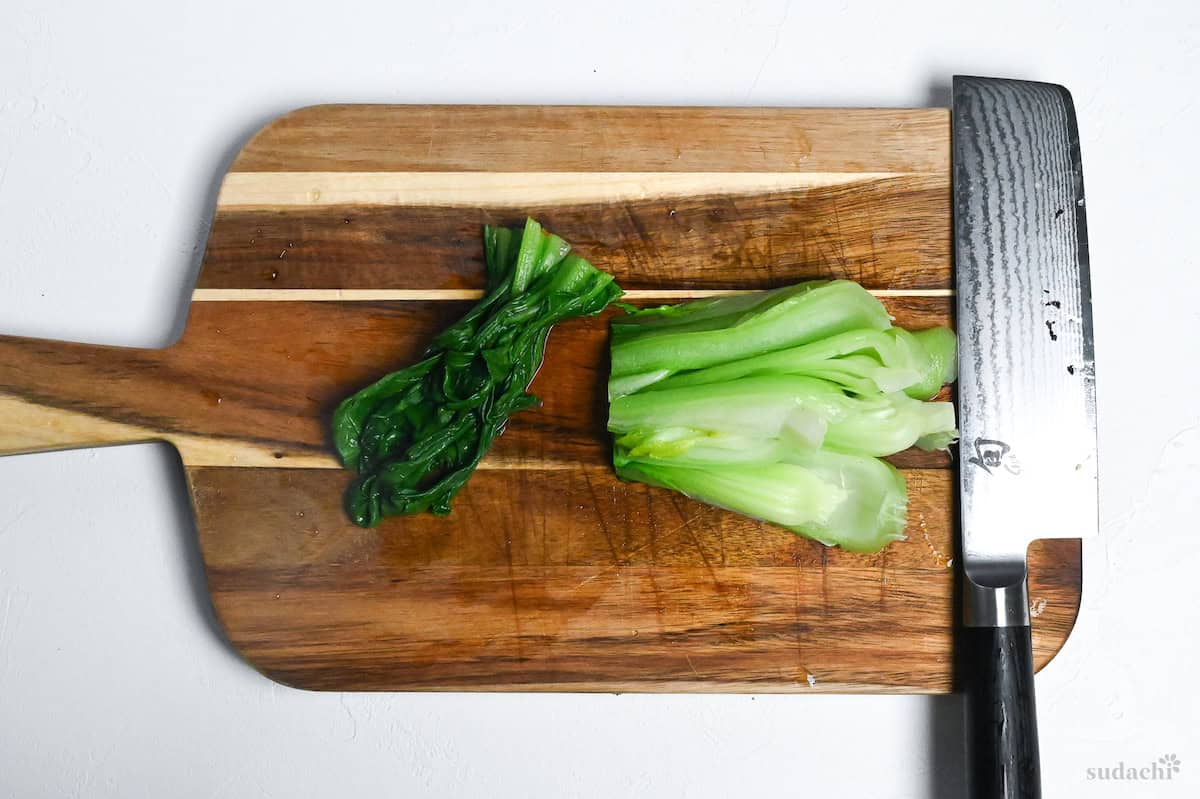 cut leaves and steams of bok choy on a wooden chopping board with Japanese knife