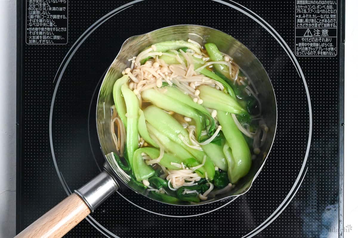 Bok choy and enoki mushrooms in broth in a saucepan on the stovetop