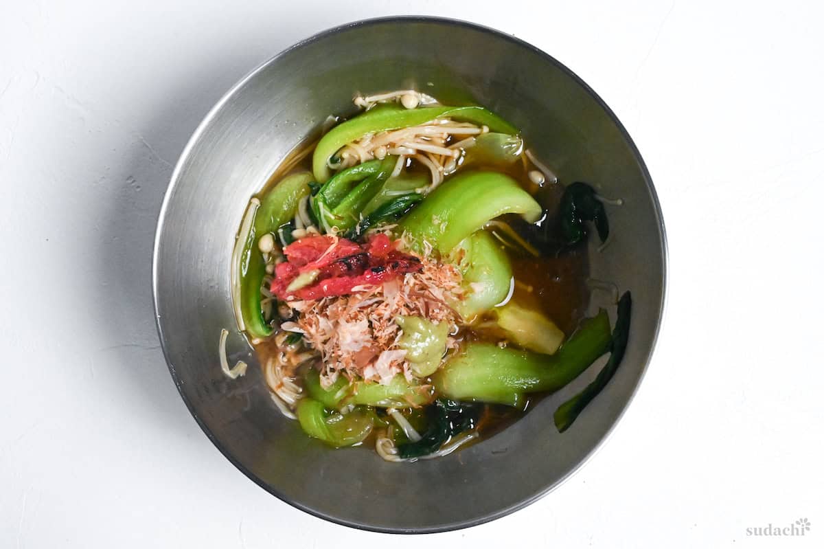 Bok choy and enoki mushrooms in broth in a mixing bowl with pasted umeboshi and bonito flakes