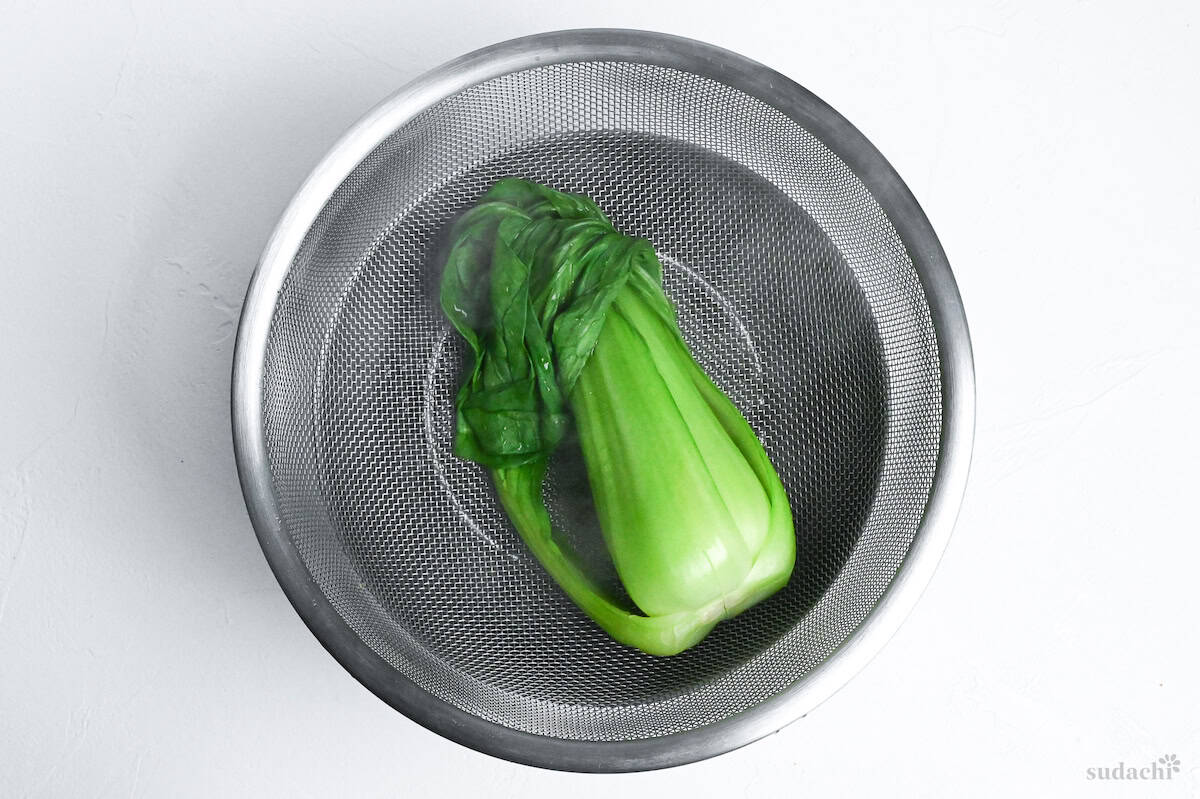 cooked bok choy in a metal sieve over a bowl on a white background