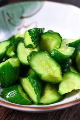 Japanese wasabi pickled cucumbers in a white dish with chopsticks and a tube of wasabi paste