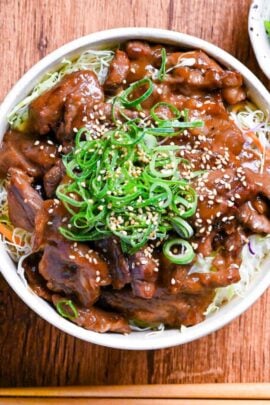 wasabi teriyaki beef over rice in a cream colored bowl and topped with green onions and sesame seeds