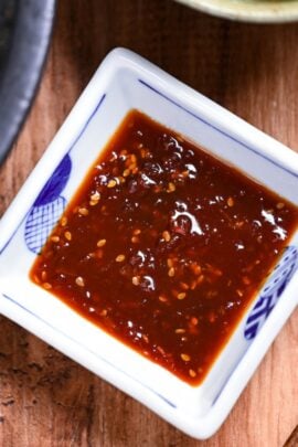 Homemade Japanese yakiniku sauce in a small square white bowl with blue border next to slices of thinly sliced beef on a metal grill