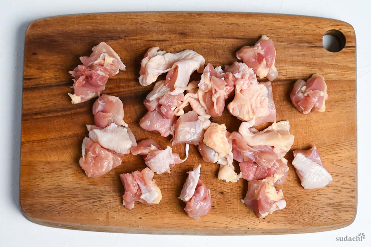 raw chicken thigh cut into bitesize pieces on a wooden chopping board ready to make homemade yakitori chicken skewers