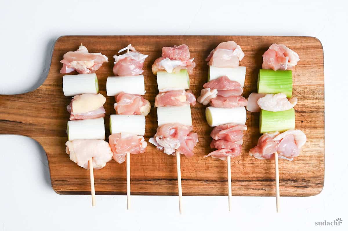 chicken thigh and Japanese leek pieces threaded onto bamboo skewers arranged on a wooden chopping board