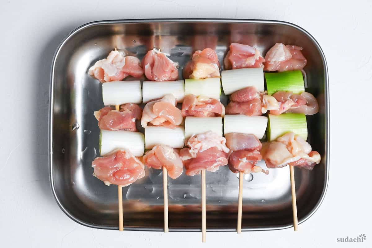 5 negima yakitori Japanese chicken and leek skewers uncooked and sprinkled with sake in a steel container