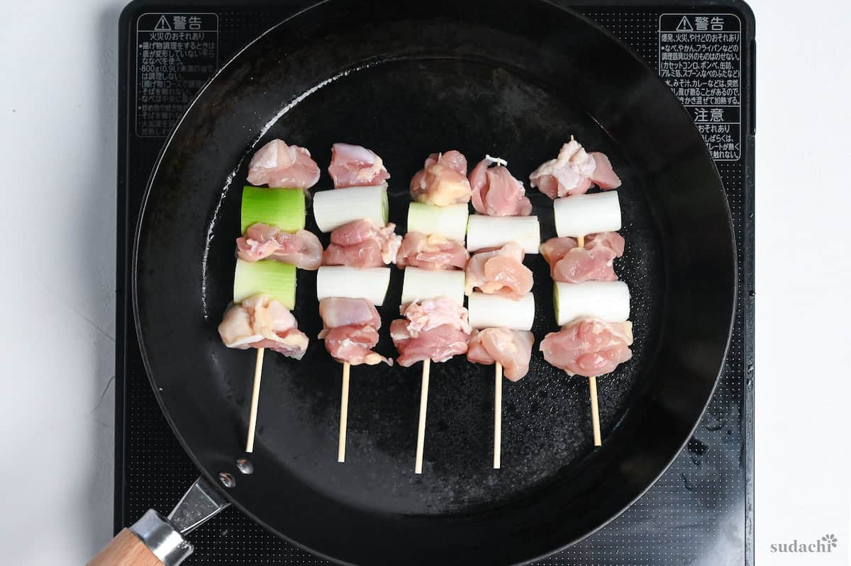 5 negima yakitori Japanese chicken and leek skewers cooking in a frying pan on the stove