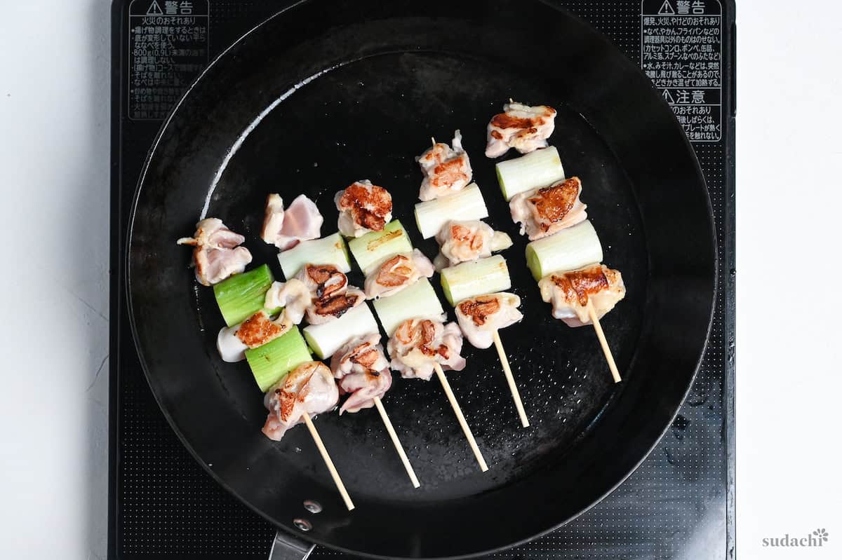 5 negima yakitori Japanese chicken and leek skewers cooking in a frying pan on the stove