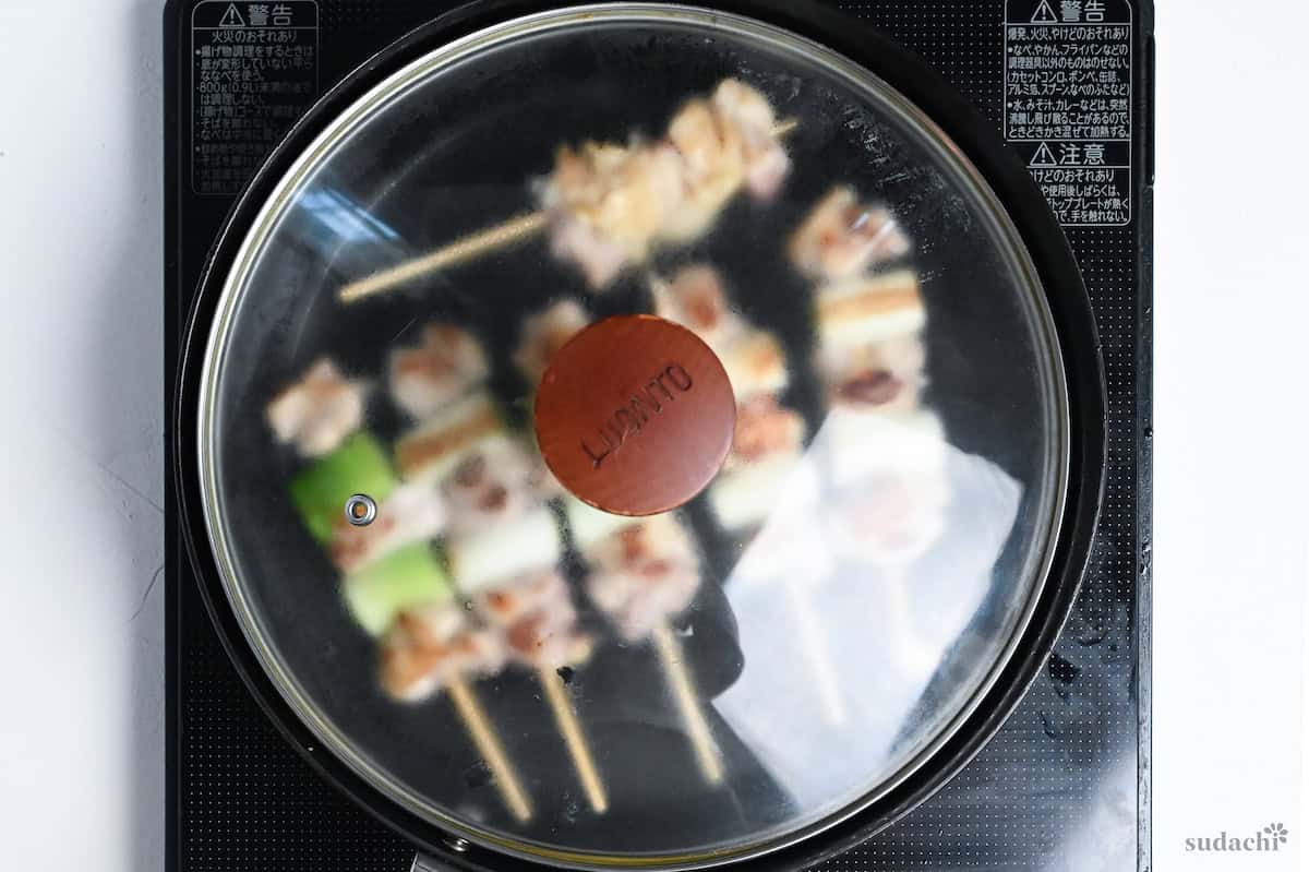 steaming yakitori skewers in a frying pan with a lid