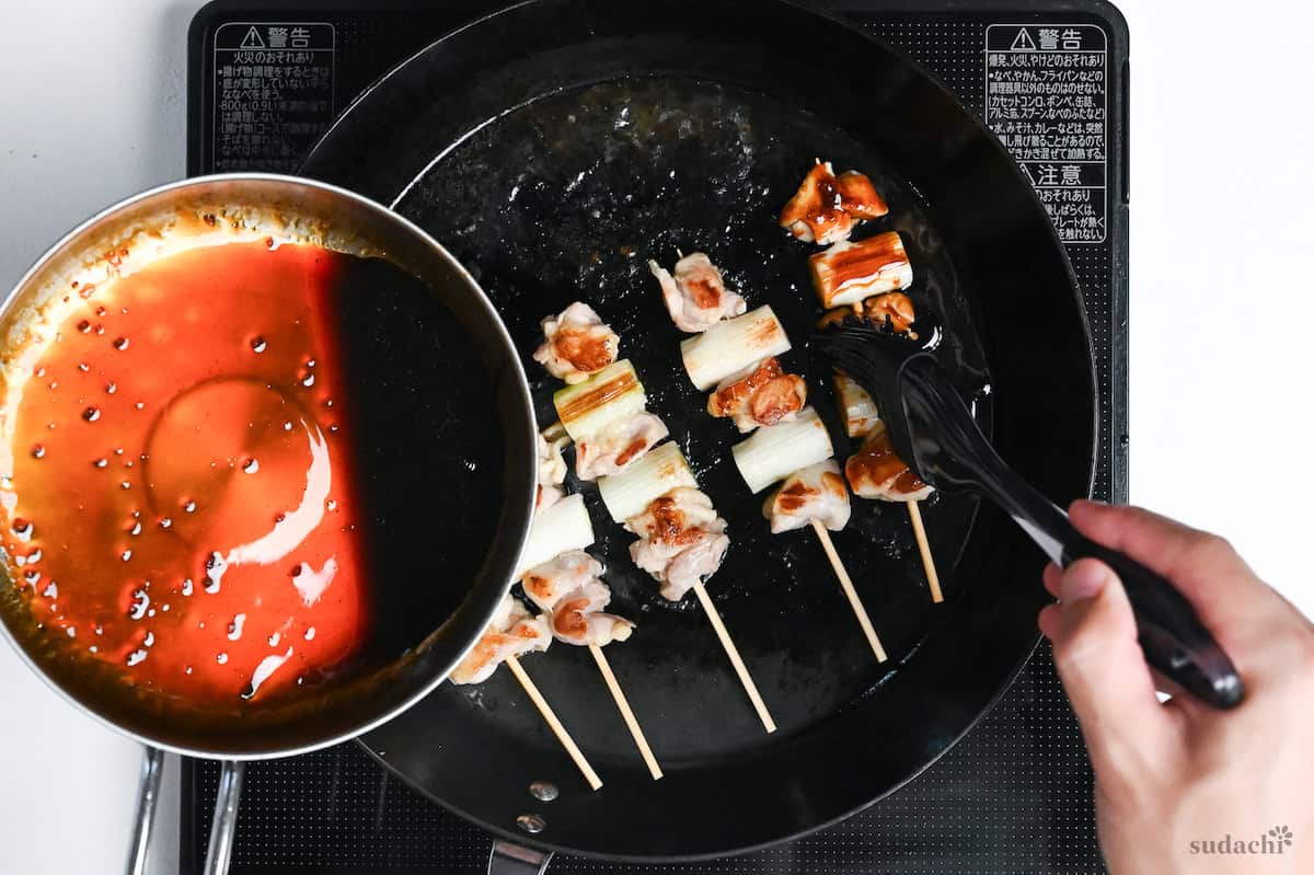 Brushing 5 negima yakitori Japanese chicken and leek skewers in a frying pan with homemade yakitori sauce