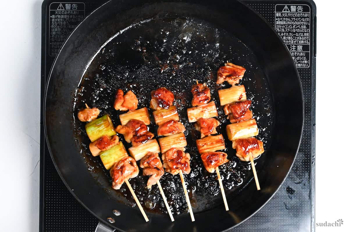 5 negima yakitori Japanese chicken and leek skewers coated in homemade sauce in a frying pan