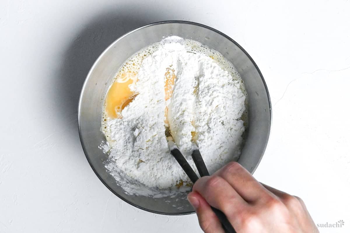 egg, water and flour in a bowl, drawing crosses in the mixture with chopsticks to make tempura batter