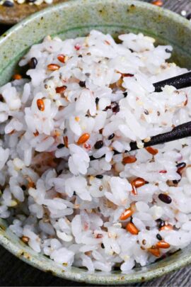 Japanese multigrain rice (zakkokumai) in a green and brown ceramic rice bowl surrounded by various grains and seeds