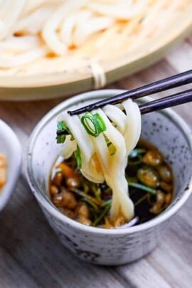 dipping cold udon noodles in mentsuyu (noodle dipping sauce) mixed with green onions