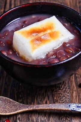 Zenzai (Japanese red bean soup) served in a black bowl and topped with toasted kirimochi