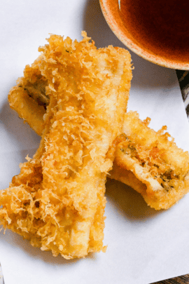 two pieces of conger eel tempura on a rectangular plate with tempura dipping sauce and grated daikon on a perilla leaf